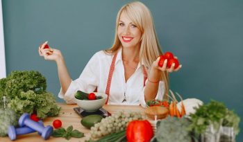 Healthy lifestyle concept with woman holding tomatoes and surrounded by fresh vegetables in a studio setting.