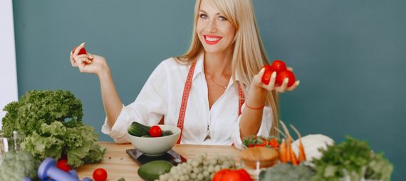 Healthy lifestyle concept with woman holding tomatoes and surrounded by fresh vegetables in a studio setting.